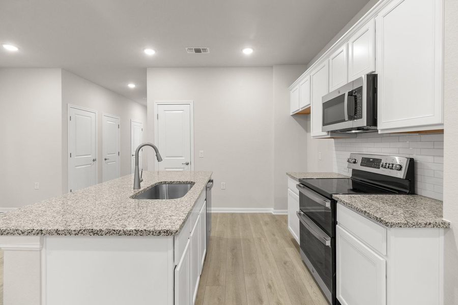 The kitchen features a large island with granite countertops and an undermount sink, white cabinetry, stainless steel appliances, and a subway tile backsplash