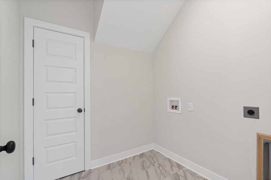 Laundry room featuring vaulted ceiling, hookup for a washing machine, electric dryer hookup, and light marble finish flooring Laundry room featuring vaulted ceiling, hookup for a washing machine, electric dryer hookup, and light marble finish flooring