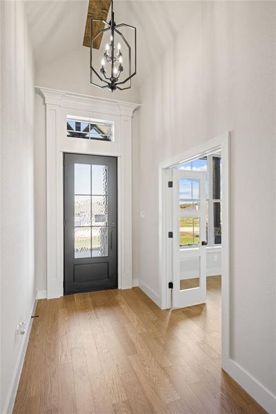 Foyer with light wood-style floors, a chandelier, healthy amount of natural light, and vaulted ceiling