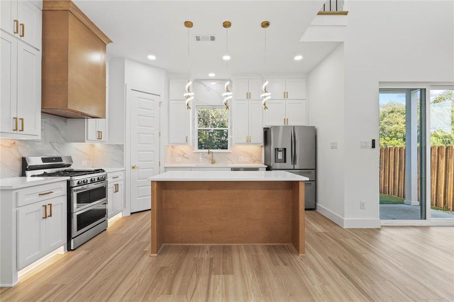 Kitchen with appliances with stainless steel finishes, a kitchen island, hanging light fixtures, decorative backsplash, and white cabinets