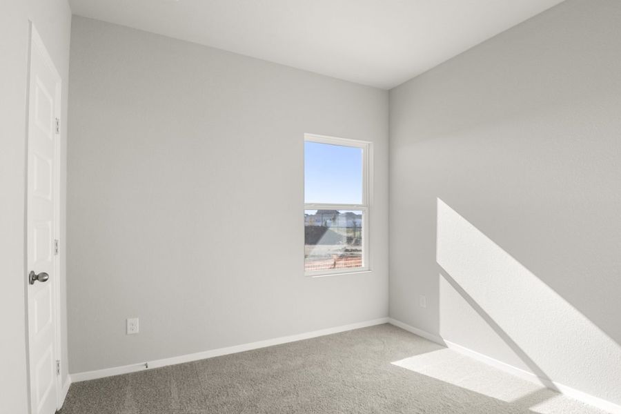 Image of a bedroom with light grey walls, tan carpeting and a window