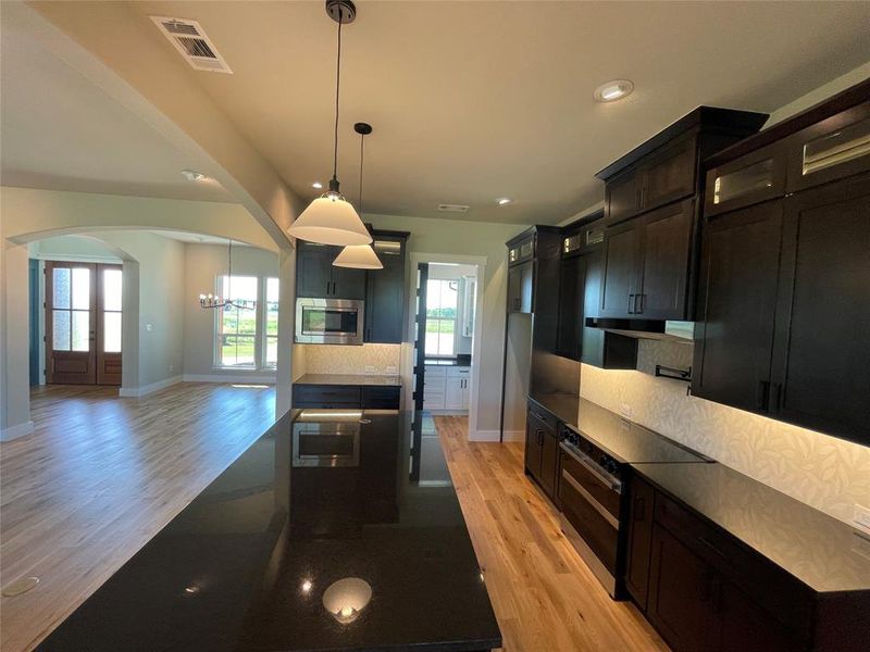 Spacious kitchen featuring an expansive island with a dark countertop, dark wood cabinetry, stainless steel appliances, and wood-finish flooring