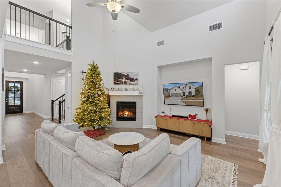 Living room featuring high vaulted ceiling, a tiled fireplace, ceiling fan, light wood-type flooring, and stairs Living room featuring high vaulted ceiling, a tiled fireplace, ceiling fan, light wood-type flooring, and stairs