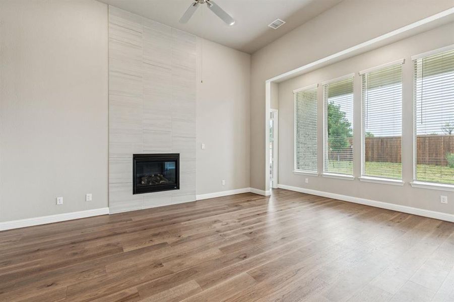 Unfurnished living room with a ceiling fan, wood finished floors, and a tile fireplace
