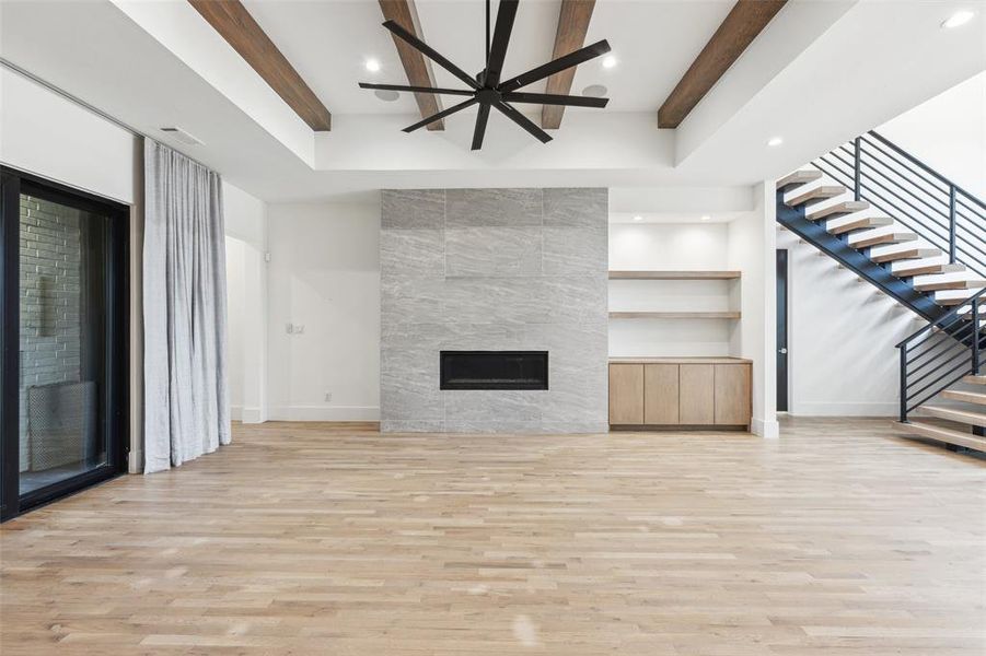 Unfurnished living room with ceiling fan, a fireplace, beamed ceiling, and light hardwood / wood-style flooring