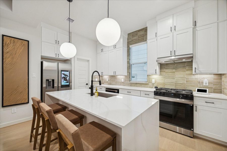 Large waterfall-edge island anchors the kitchen, offering generous workspace and seating. Matte black fixtures, quartz surfaces, and subtle tile accents lend a polished, modern aesthetic while maintaining a comfortable, inviting feel that connects seamlessly to the living area.