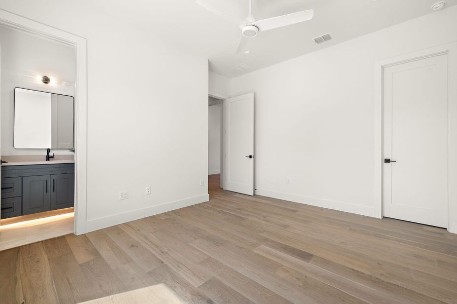 Unfurnished bedroom featuring light wood finished floors, visible vents, ensuite bathroom, a sink, and baseboards