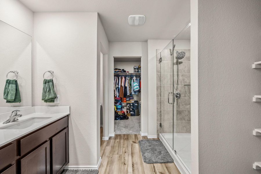 A streamlined primary bathroom features a spacious glass shower and dual vanity, leading to a walk-in closet.