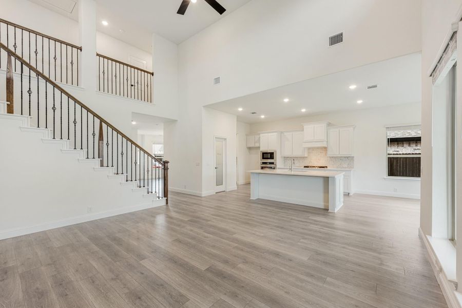 Open-concept living area with two-story ceiling, staircase, and white kitchen with island and hardwood floors