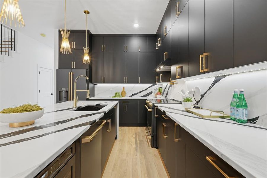 Kitchen with stainless steel appliances, pendant lighting, light wood finished floors, and dark cabinetry