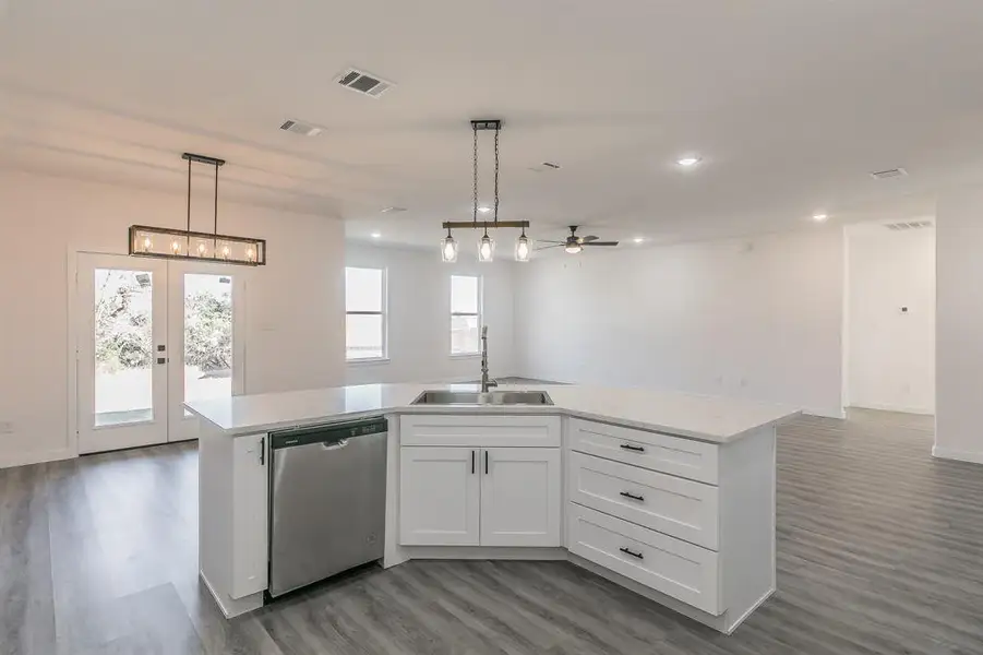 Kitchen with visible vents, dishwasher, open floor plan, a kitchen island with sink, and a sink