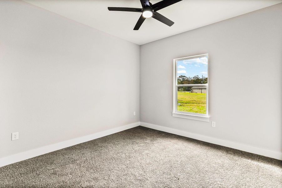 This room features fresh, neutral walls and plush carpeting, with a large window offering plenty of natural light and views of the outdoors. A modern ceiling fan adds comfort and style. This room features fresh, neutral walls and plush carpeting, with a large window offering plenty of natural light and views of the outdoors. A modern ceiling fan adds comfort and style.