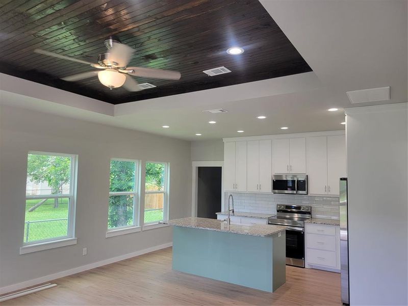 Open-concept living area featuring a kitchen island with stone-finish countertop, white shaker cabinetry, stainless steel appliances, and a subway tile backsplash
