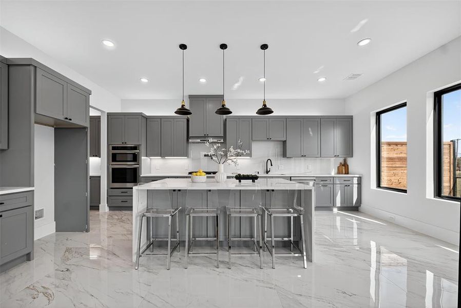 Kitchen featuring gray cabinetry, light stone countertops, decorative light fixtures, a kitchen bar, and a center island