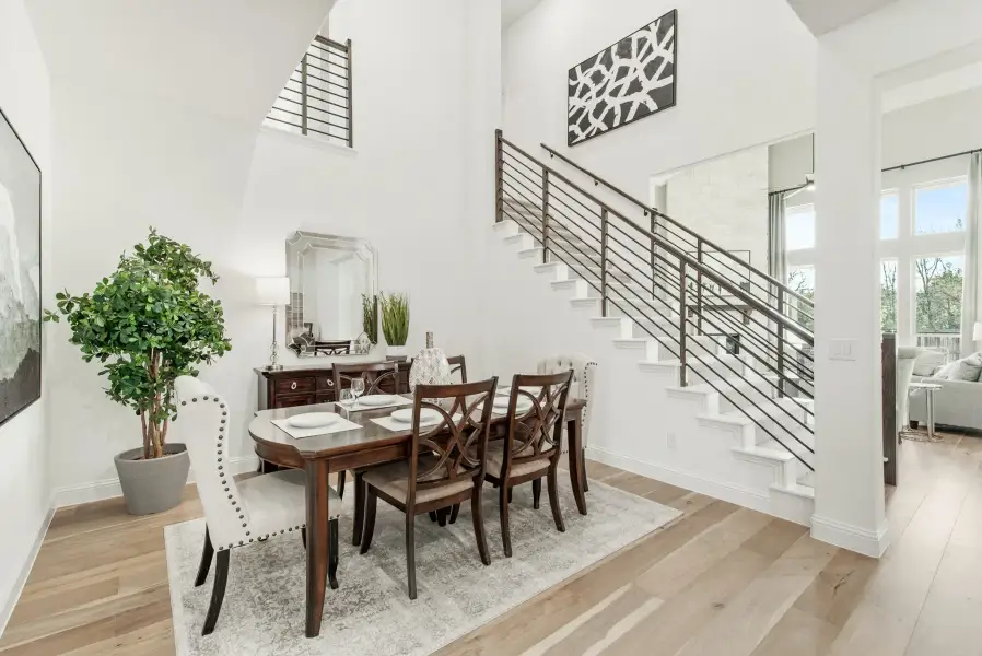 Dining room with two-story ceiling, wood table and chairs, and staircase with metal railing