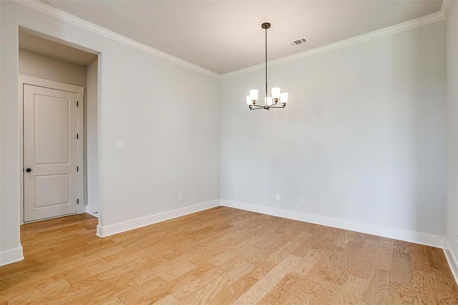 Empty room with an inviting chandelier, ornamental molding, and light hardwood / wood-style floors