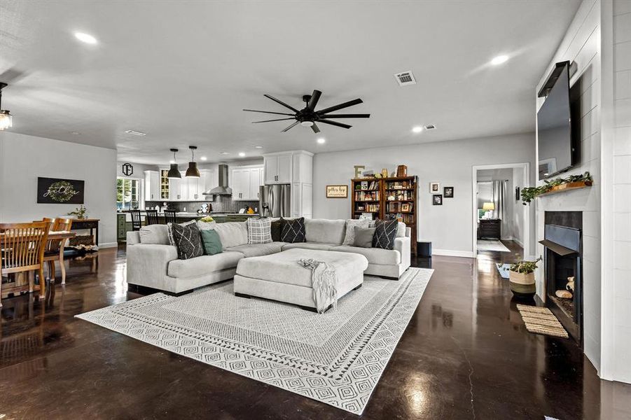 Living room with recessed lighting, concrete flooring, a tiled fireplace, and ceiling fan Living room with recessed lighting, concrete flooring, a tiled fireplace, and ceiling fan