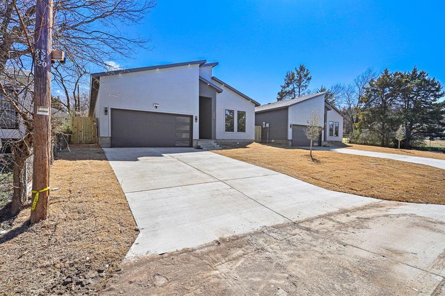 View of front of property featuring an attached garage, driveway, fence, and stucco siding