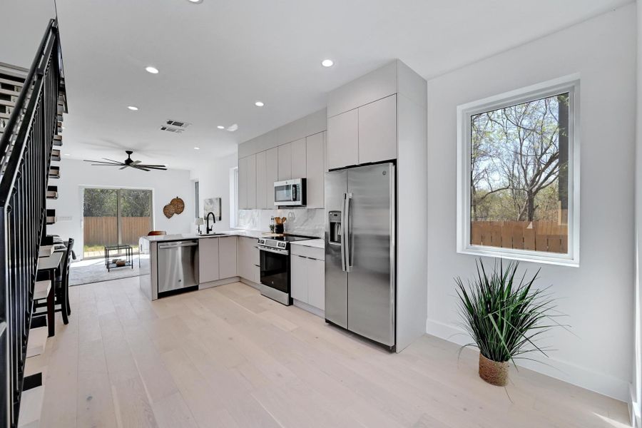 Kitchen with modern cabinets, a sink, stainless steel appliances, light wood-style floors, and a peninsula