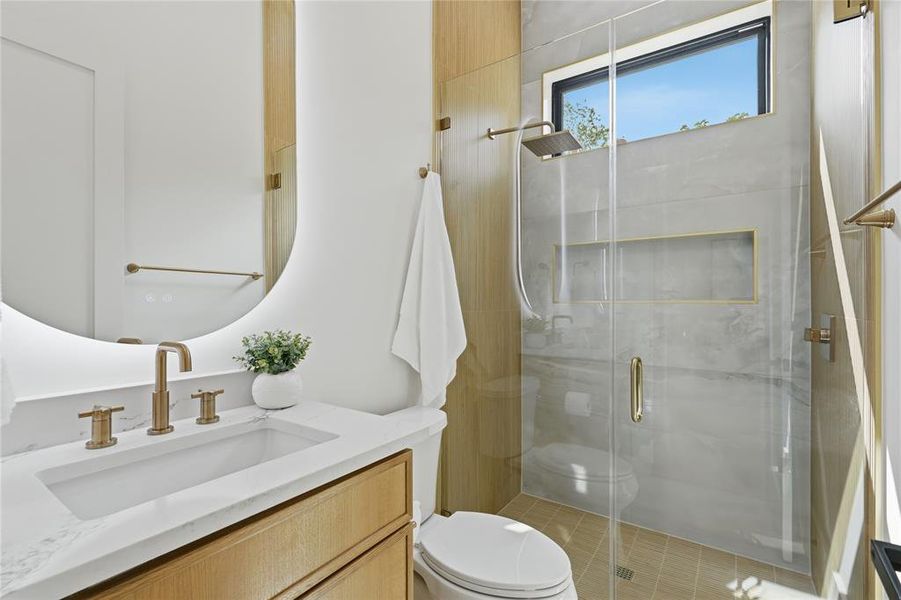 Bathroom featuring a wood-finish vanity with a white countertop and integrated sink, circular illuminated mirror, and brass-finish fixtures Bathroom featuring a wood-finish vanity with a white countertop and integrated sink, circular illuminated mirror, and brass-finish fixtures