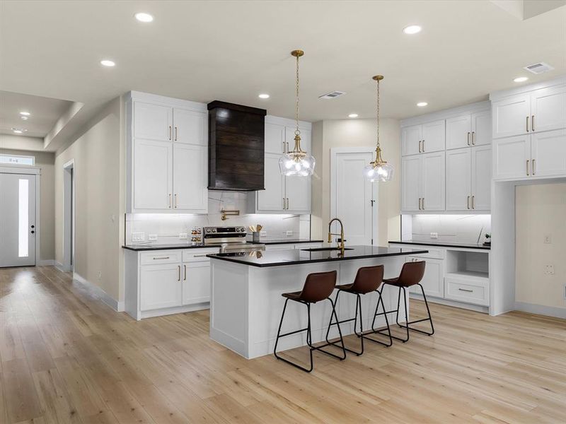 Modern kitchen featuring a central island, contrasting dark countertops, extensive white cabinetry, recessed lighting, and wood-finish flooring