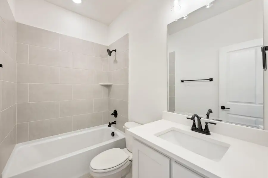 Bathroom with tiled tub-shower combo, white vanity with black fixtures, and toilet