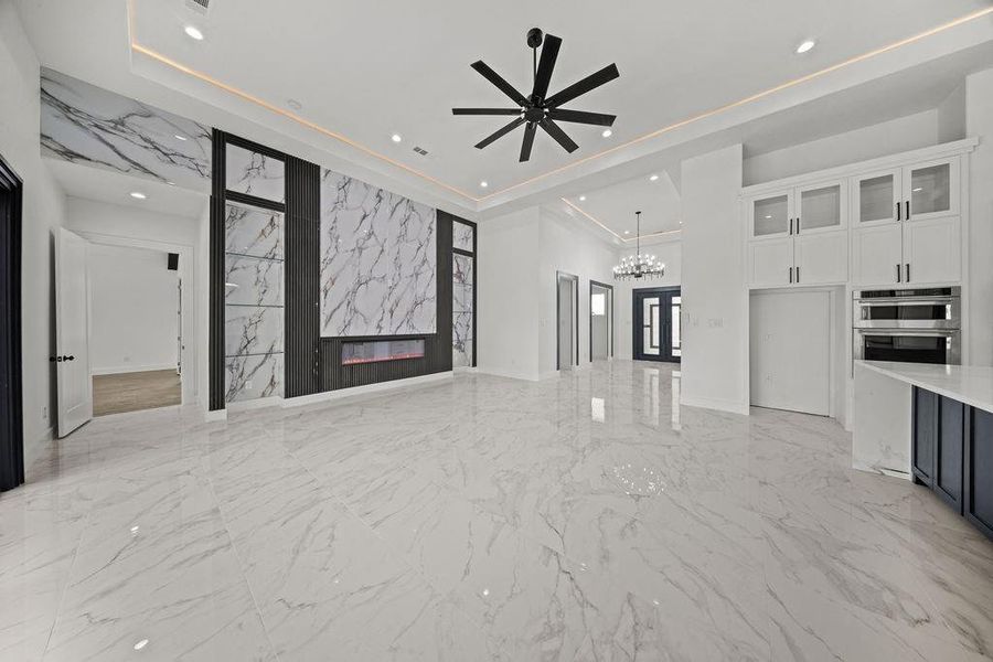 Unfurnished living room with a ceiling fan, a high end fireplace, a tray ceiling, light marble finish floors, and suspended lighting