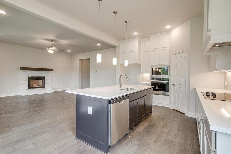 Kitchen featuring a stone fireplace, appliances with stainless steel finishes, a kitchen island with sink, sink, and ceiling fan