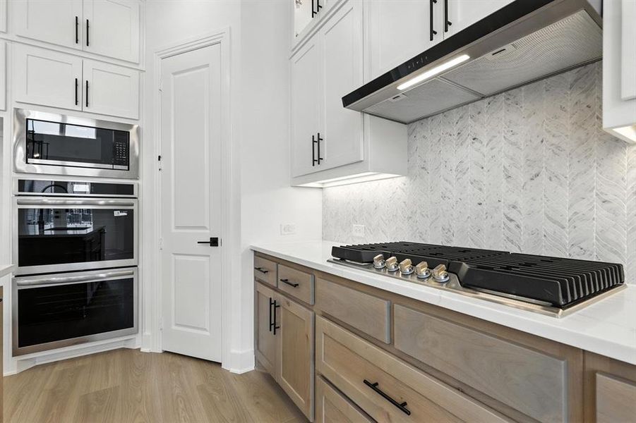 Kitchen with light wood-style floors, appliances with stainless steel finishes, white cabinets, under cabinet range hood, and backsplash Kitchen with light wood-style floors, appliances with stainless steel finishes, white cabinets, under cabinet range hood, and backsplash