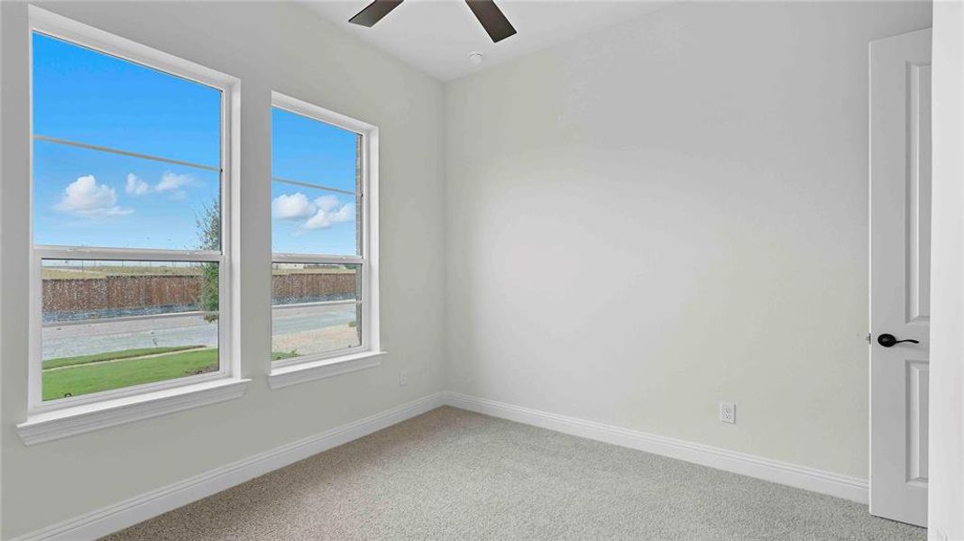 Bright room featuring two large windows, neutral-toned carpeting, white baseboards, and a ceiling fan with a dark finish