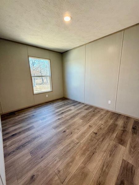 Unfurnished room with a decorative wall, light wood finished floors, and a textured ceiling Unfurnished room with a decorative wall, light wood finished floors, and a textured ceiling