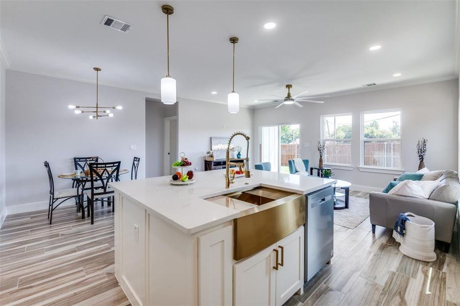 Kitchen featuring light wood-type flooring, a center island with sink, dishwasher, and ornamental molding