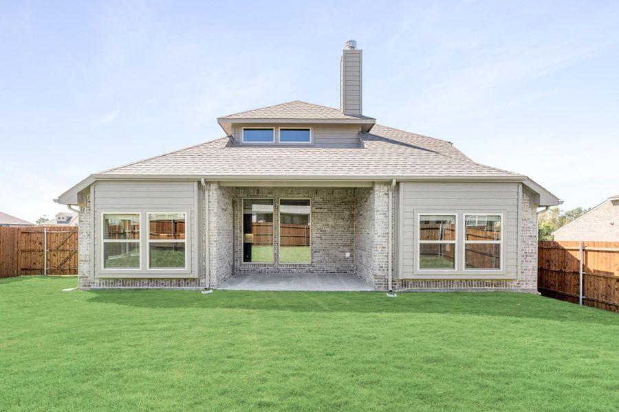Rear exterior of brick home with covered patio, chimney, and fenced backyard with green lawn Rear exterior of brick home with covered patio, chimney, and fenced backyard with green lawn