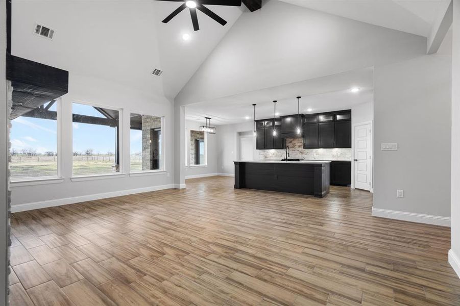 Unfurnished living room featuring beam ceiling, high vaulted ceiling, and ceiling fan with notable chandelier