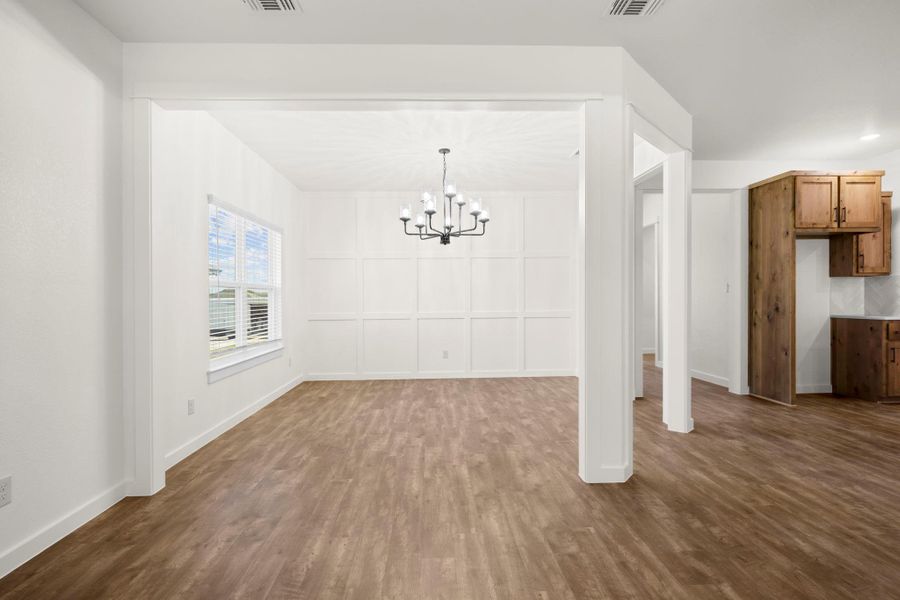 A classic chandelier illuminates the formal dining space, featuring tasteful wall paneling and durable wood flooring.