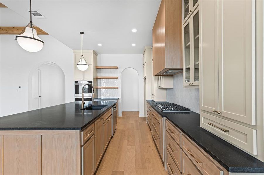 Kitchen featuring arched walkways, a kitchen island with sink, light wood finished floors, glass insert cabinets, and two tone color scheme