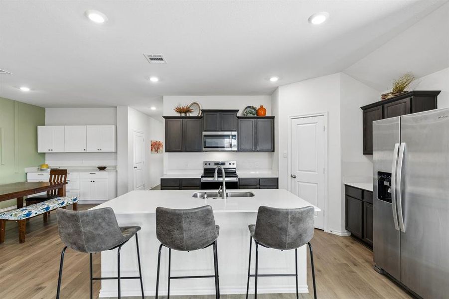 Kitchen featuring stainless steel appliances, a kitchen island with sink, light wood-type flooring, a breakfast bar, and recessed lighting Kitchen featuring stainless steel appliances, a kitchen island with sink, light wood-type flooring, a breakfast bar, and recessed lighting