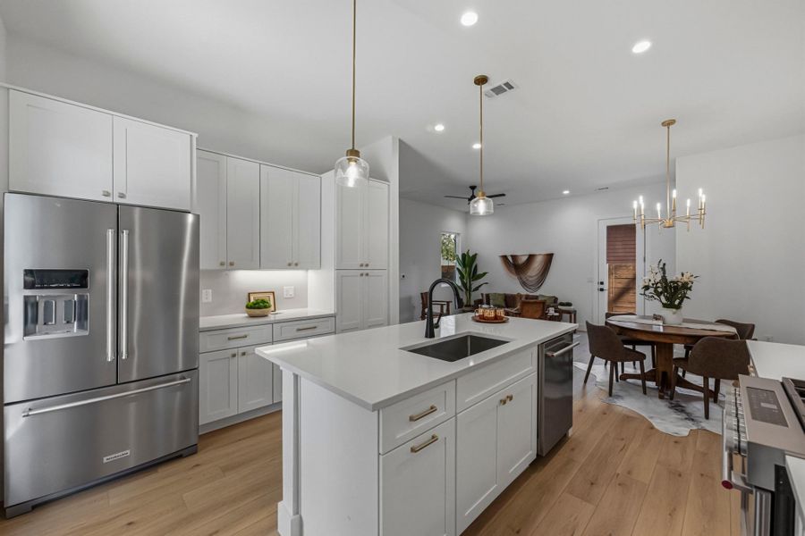 Kitchen featuring high quality appliances, a ceiling fan, white cabinetry, light wood-type flooring, and a kitchen island with sink