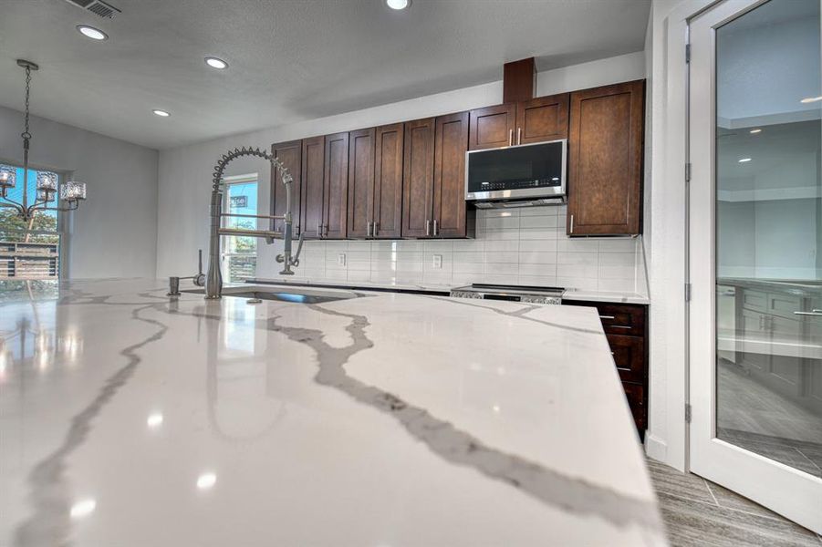 Kitchen featuring appliances with stainless steel finishes, decorative backsplash, light stone counters, and pendant lighting