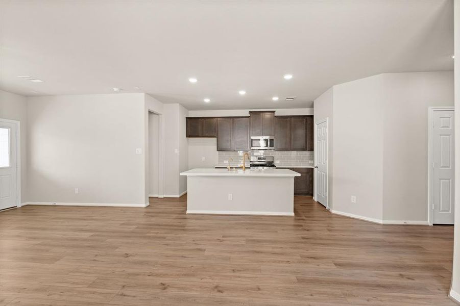 This light and bright kitchen features a large quartz island, dark stained cabinets, a large sink overlooking your family room, recessed lighting, and beautiful backsplash.