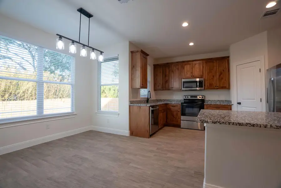 Kitchen featuring stainless steel appliances, recessed lighting, decorative light fixtures, dark stone countertops, and light wood-type flooring Kitchen featuring stainless steel appliances, recessed lighting, decorative light fixtures, dark stone countertops, and light wood-type flooring