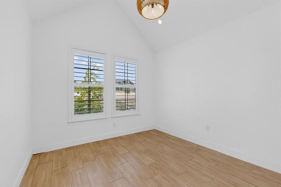 Vaulted ceiling room featuring two windows with plantation shutters, wood-finish flooring, and a decorative ceiling light fixture Vaulted ceiling room featuring two windows with plantation shutters, wood-finish flooring, and a decorative ceiling light fixture