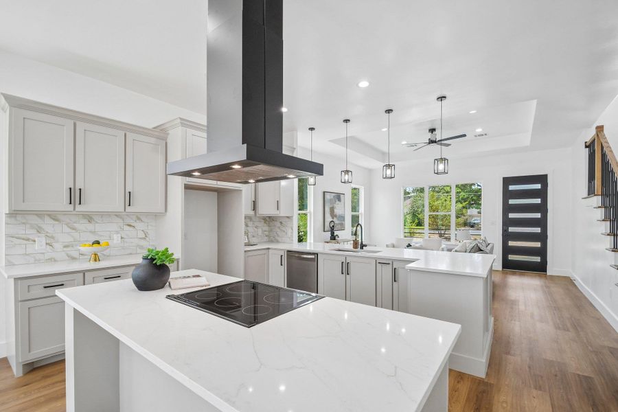 An open kitchen displays quartz countertops, light gray cabinetry, and a modern island cooktop. An open kitchen displays quartz countertops, light gray cabinetry, and a modern island cooktop.