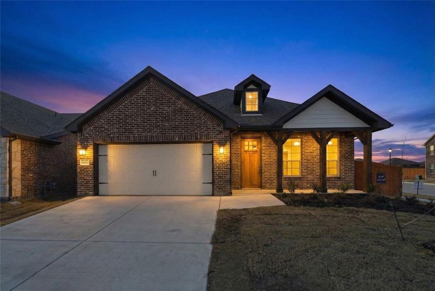 View of front of house with an attached garage, brick siding, concrete driveway, and a porch