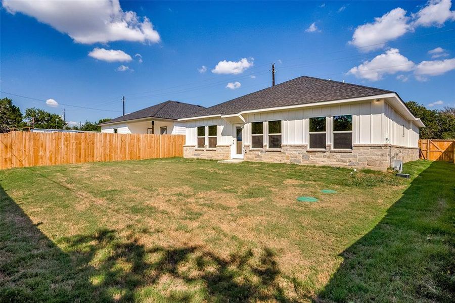 Back of property featuring a fenced backyard, roof with shingles, board and batten siding, a patio area, and stone siding Back of property featuring a fenced backyard, roof with shingles, board and batten siding, a patio area, and stone siding