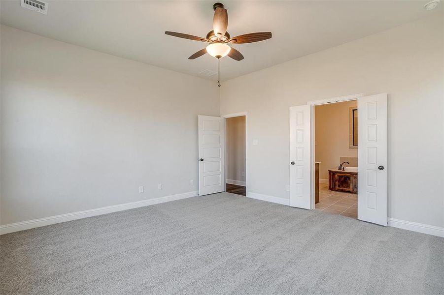 Unfurnished bedroom featuring ceiling fan, connected bathroom, and light carpet