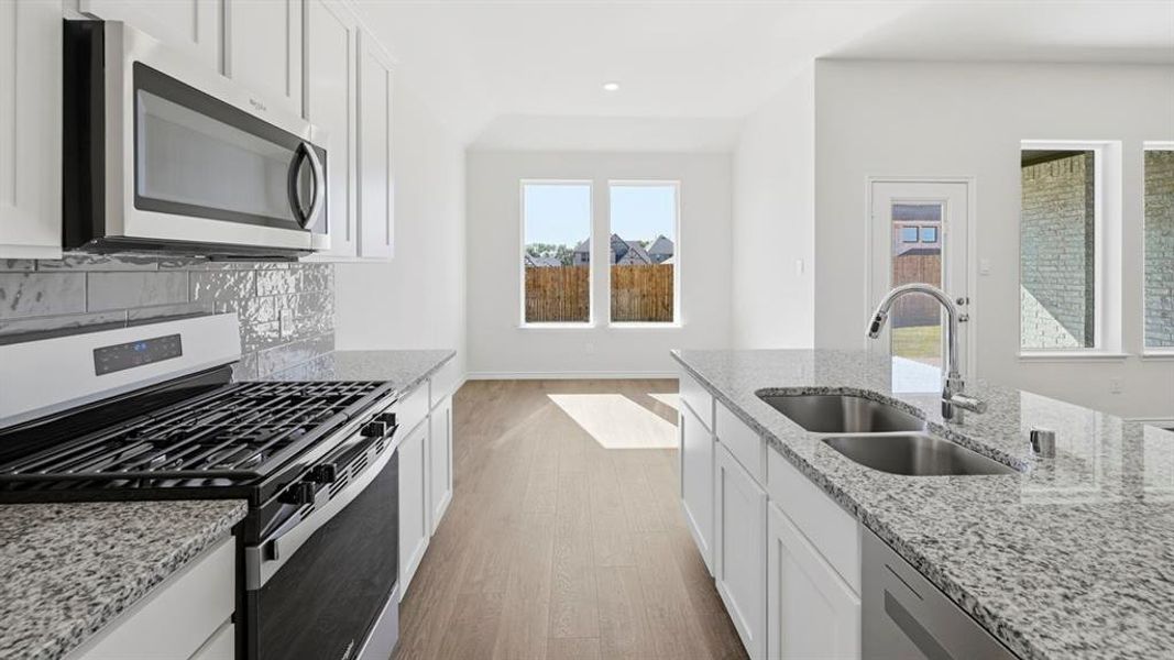 Modern kitchen featuring white cabinetry, granite countertops, stainless steel appliances, a gas range, and a double basin sink Modern kitchen featuring white cabinetry, granite countertops, stainless steel appliances, a gas range, and a double basin sink
