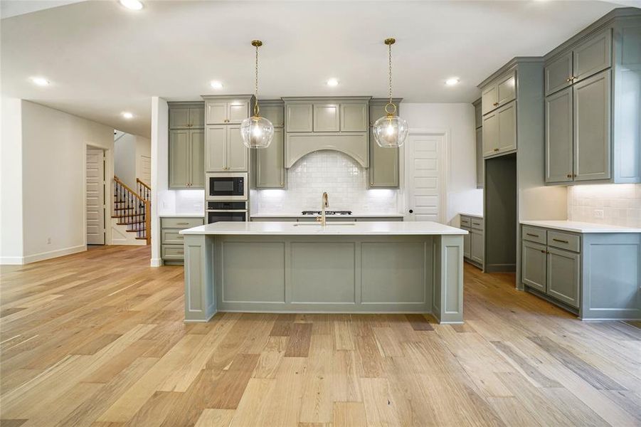 Kitchen with hanging light fixtures, light stone counters, light wood finished floors, oven, and built in microwave