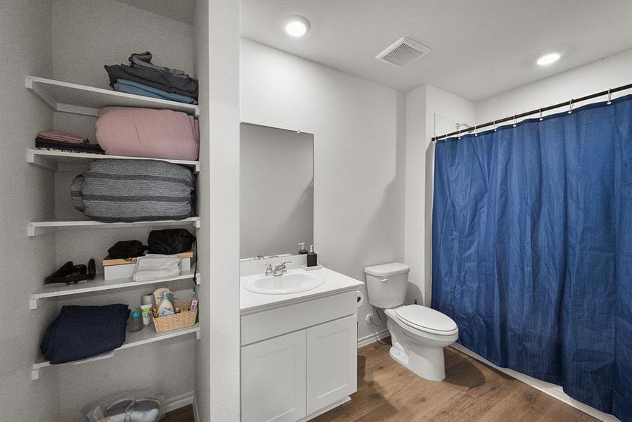 Bathroom featuring wood-finish flooring, a white vanity with an integrated sink, a toilet, and a shower with a blue curtain