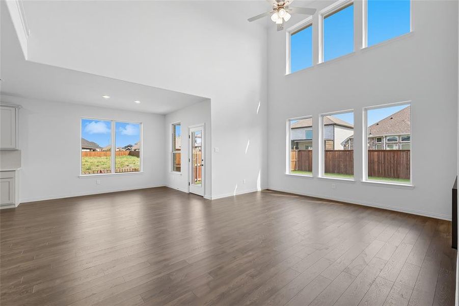 Unfurnished living room featuring plenty of natural light, dark wood-style floors, a high ceiling, and a ceiling fan Unfurnished living room featuring plenty of natural light, dark wood-style floors, a high ceiling, and a ceiling fan
